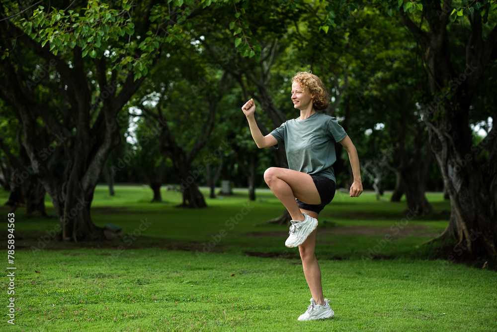 A young girl, of European appearance, with blond hair, is doing morning exercises in the fresh air in a park on the grass.