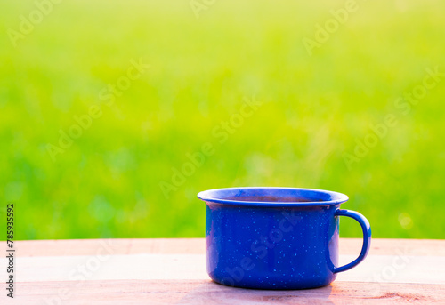 cup of coffee, blue enamel coffee mugs On an old wooden floor, Blurred background of rice fields at sunrise.