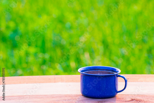 cup of coffee, blue enamel coffee mugs On an old wooden floor, Blurred background of rice fields at sunrise.