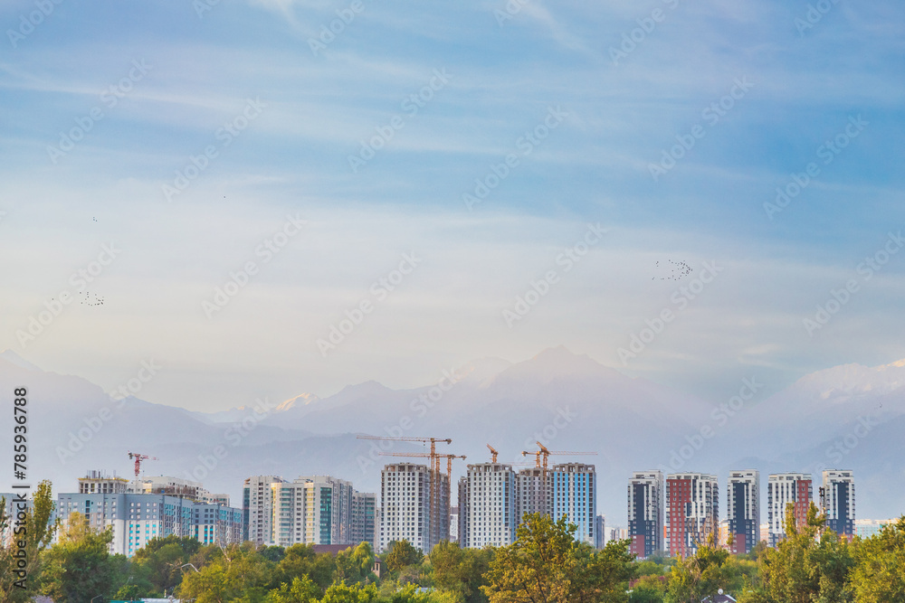 Fototapeta premium Dense development of the city of Almaty with high-rise residential complexes against the backdrop of mountains in a seismic zone, copy space