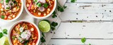 Vibrant overhead shot of two bowls of pozole, a classic Mexican soup with flavorful toppings, on withe boards.