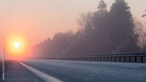 Sunrise, in the foreground, the road passing through the forest is covered with a thin layer of fog