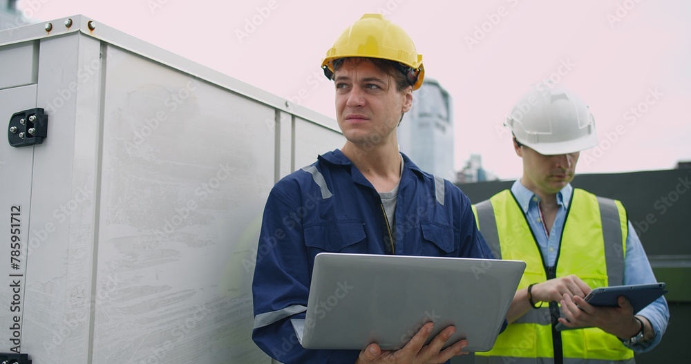 civil engineer Construction manager and manual worker inspector foreman in safety helmet holding laptop meeting conversation about project work at rooftop of building construction site civil engineer Construction manager and manual worker inspector foreman in safety helmet holding laptop meeting conversation about project work at rooftop of building construction site