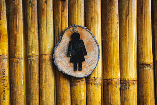 Sign symbol WOMEN on the door of a public toilet with a background of arranged wood and bamboo. Restroom sign on a toilet door. Women WC signs for restroom. 
