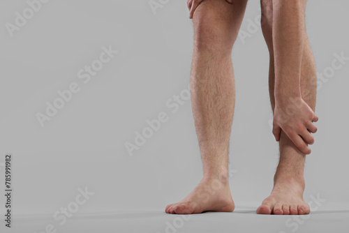 Man suffering from leg pain on grey background, closeup. Space for text