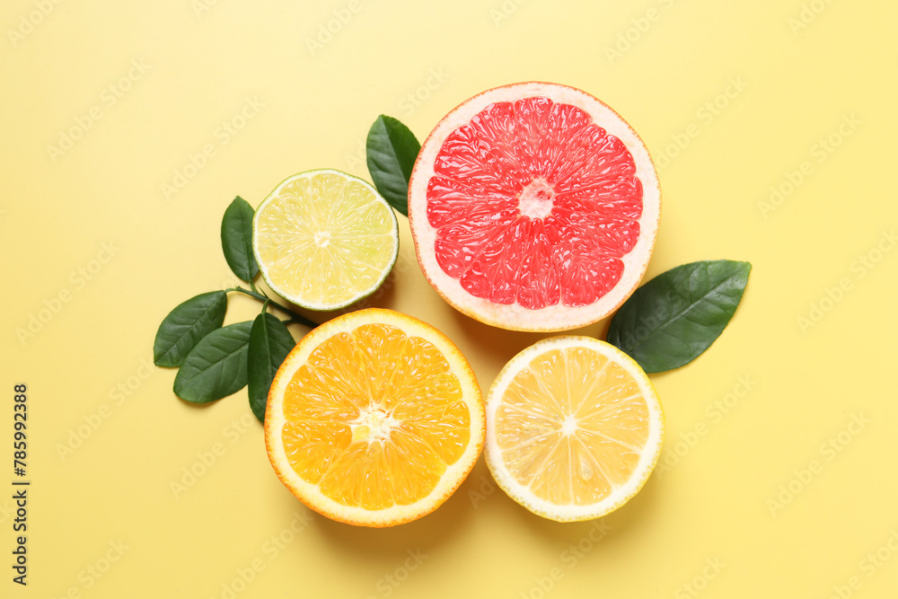 Different cut citrus fruits and leaves on yellow table, flat lay