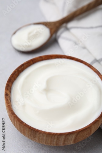 Delicious natural yogurt in bowl and spoon on light grey table, closeup