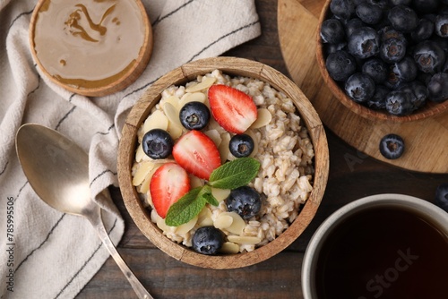Tasty oatmeal with strawberries, blueberries and almond petals served on wooden table, flat lay