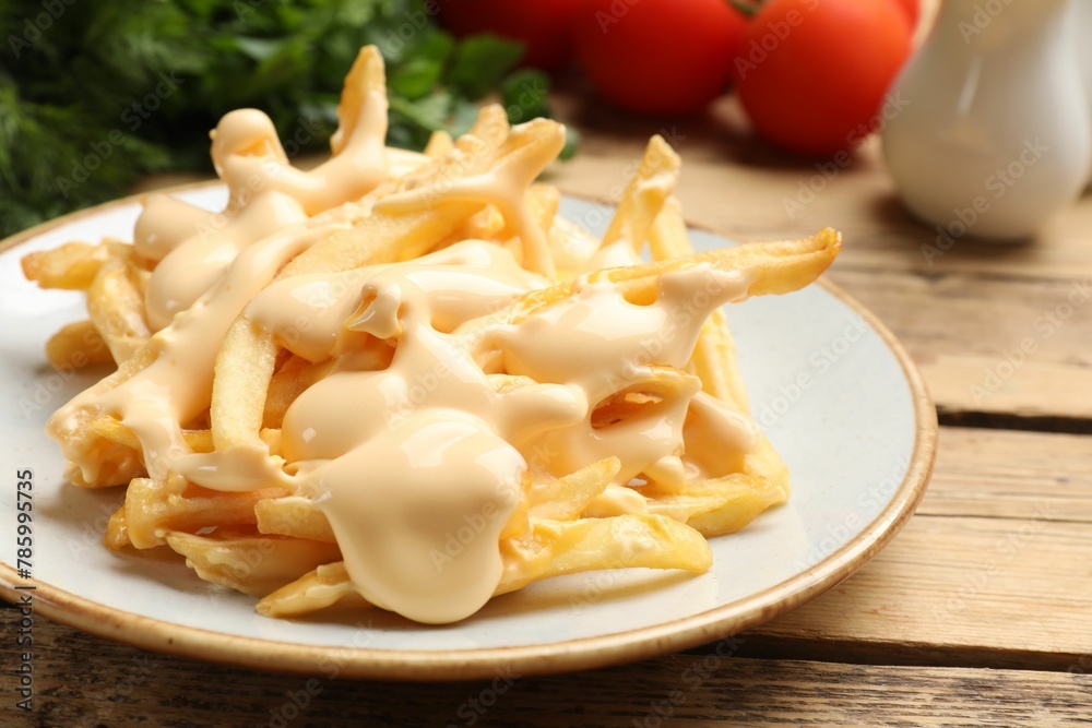 Delicious French fries with cheese sauce on wooden table, closeup