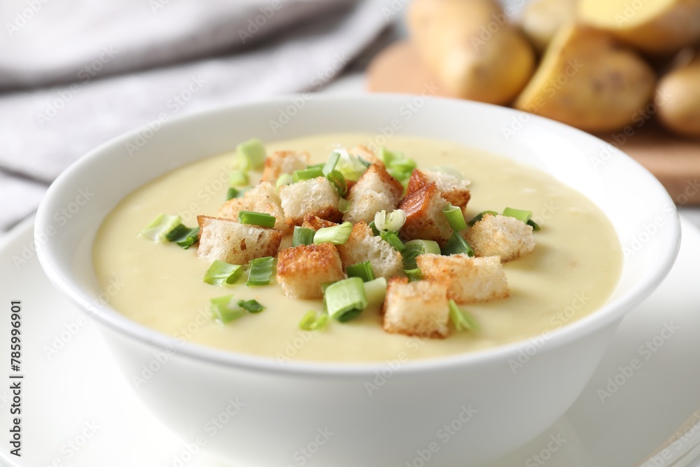 Tasty potato soup with croutons and green onion in bowl on white table, closeup