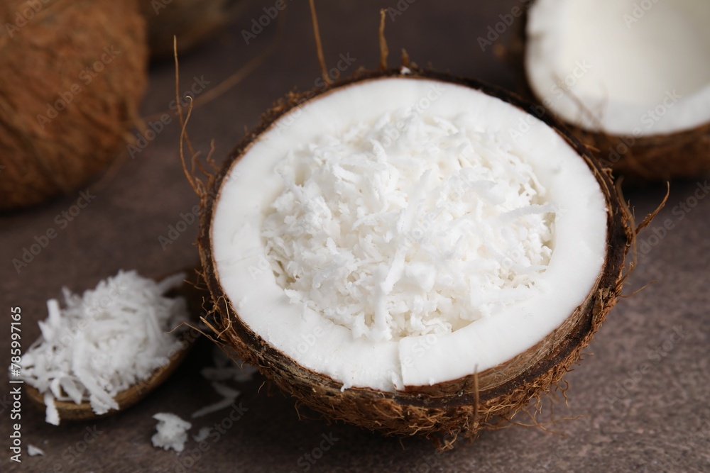 Coconut flakes in nut shell and spoon on brown table, closeup Coconut flakes in nut shell and spoon on brown table, closeup