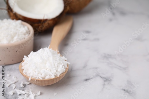 Coconut flakes in wooden spoon on white marble table, closeup. Space for text