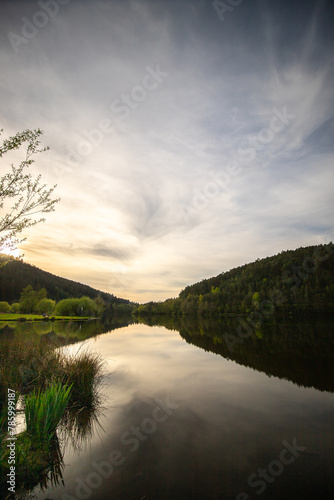 A lake in a landscape shot. A sunset and the natural surroundings are reflected in the water of the reservoir. Marbachstausee, Odenwald, Hesse photo