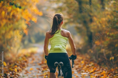 An energetic female fitness model wearing a lime green racerback top and leggings, cycling vigorously on a rural trail surrounded by autumn leaves photo