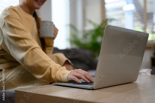 Young woman holding cup of coffee and using laptop in living room