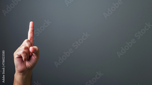 A hand with a raised index finger on a gray background, directing a close-up gesture photo