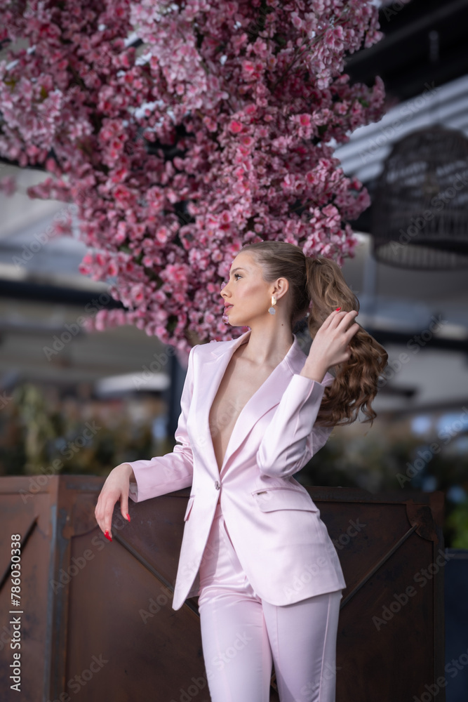 Fototapeta premium Beautiful young woman in pink suit holding her hair