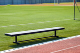 Empty bench on the sports field with green grass and red running track
