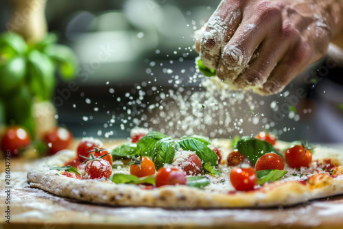 A chef applies the finishing touch to a pizza, dusting flour on top and garnishing with fresh tomatoes and basil, under the bright kitchen lights.