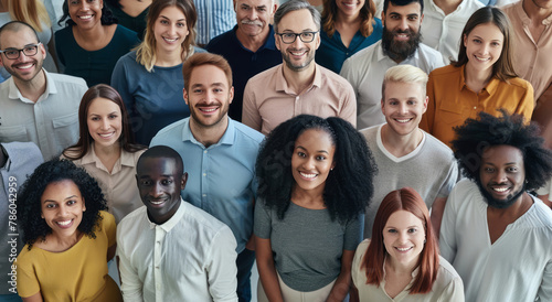 A large, diverse group of people, all standing together in an office setting, smile and look at the camera against a neutral background. photo