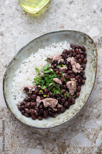 Oval bowl with black beans and rice on a light-brown granite background, vertical shot, elevated view