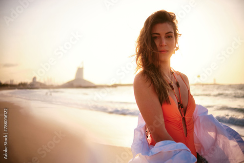 Elegant woman in swimwear with a flowing white garment on a sunset beach