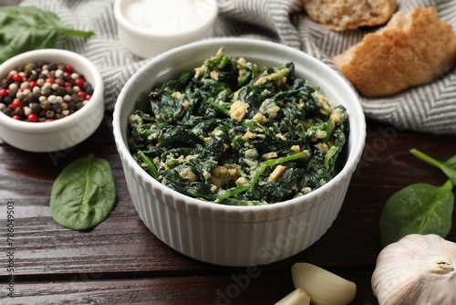 Tasty spinach dip with egg in bowl, spices and bread on wooden table, closeup
