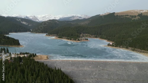 Partially frozen sweet water lake , called Bolboci lake in the Carpathians mountains , Romania , serving as a water dam , aerial view of the area at beginning of spring. photo
