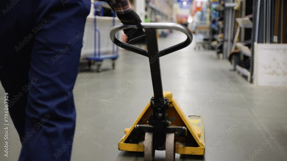A worker in a warehouse or hardware store uses a hand pallet stacker to transport pallets A worker in a warehouse or hardware store uses a hand pallet stacker to transport pallets