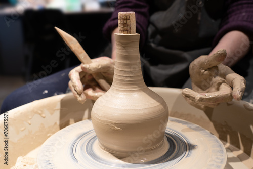 The finished clay bottle stands on a potter's wheel. There are dirty hands of a master with a tool. Close-up.