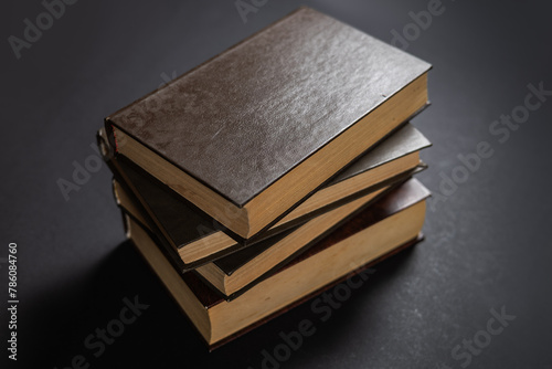 Vintage, antiquarian books pile on wooden surface in warm directional light. Selective focus photo