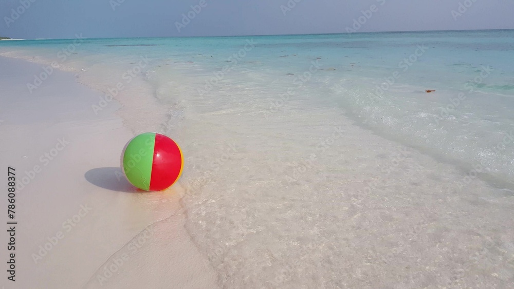 Small colorful ball on the sandy beach near the coastline Small colorful ball on the sandy beach near the coastline