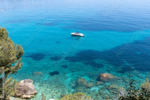 Small boat floating in a bright blue sea with the seabed visible below under bright sunlight