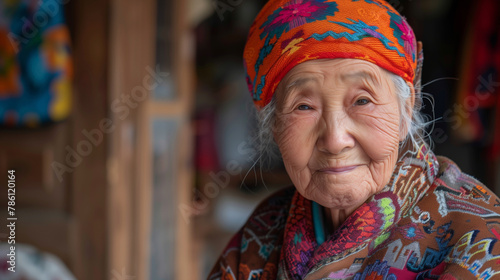 A Chinese old woman with a colorful hat and a red and white jacket. She is smiling and looking at the camera. A kind Chinese old lady with a kind smile photo