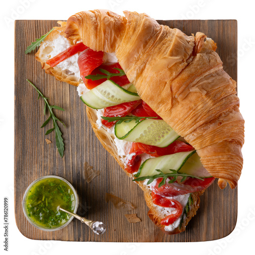 Croissant sandwich with cream cheese, smoked salmon, cucumber and arugula served with pesto on wooden board isolated on white. Top view.