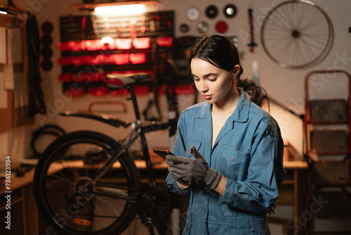 Mechanic reading a message on smartphone in bicycle workshop, she is repairing or servicing in a garage