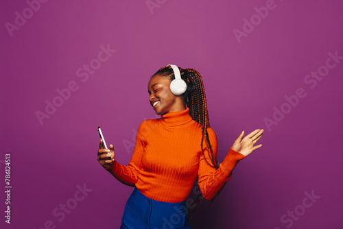 Happy girl dancing and holding a smartphone with vibrant purple background