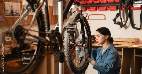 Young female mechanic fixing wheel on a bicycle during a repairman in workshop or garage. bike repair