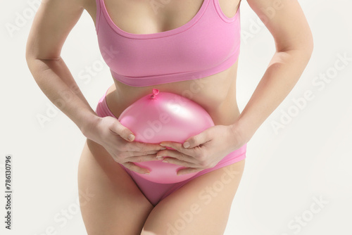 Young woman holding balloon as a sign of an stomach inflation, bloating and menstrual cramps concept 