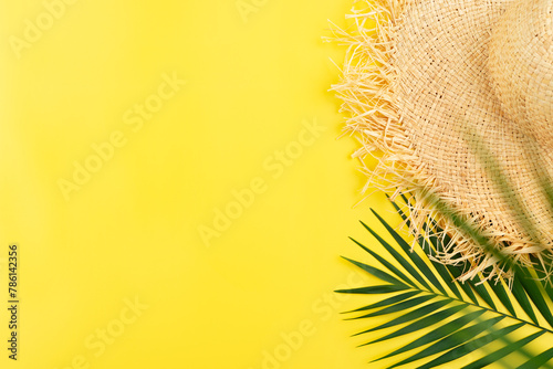 Vacation travel planning simple theme of straw hat and palm leaves on uniform yellow background flat lay with copy-space