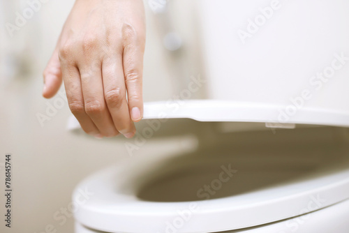 man's hand opening the toilet lid. © methaphum