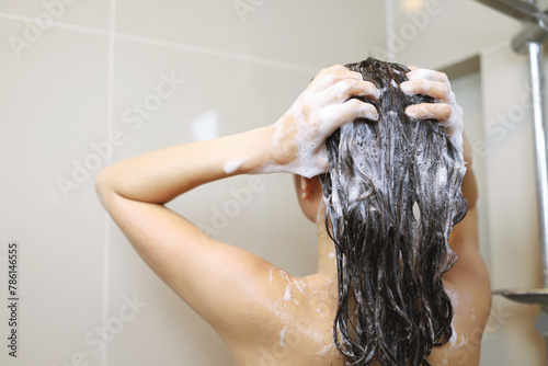 Woman is washing her hair with shampoo.