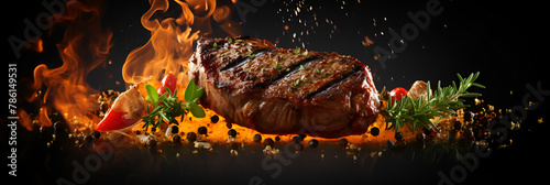 Hot grilled meat with fire, smoke and spices BBQ steaks with fresh herbs and tomatoes on black background  photo