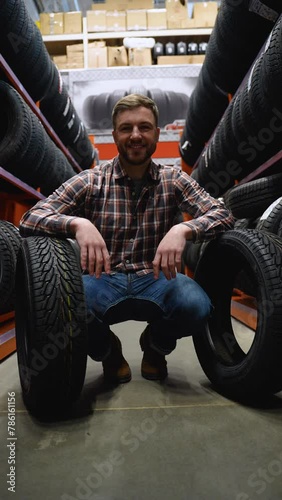 A man in a tire store with two new tires for car. Vertical video