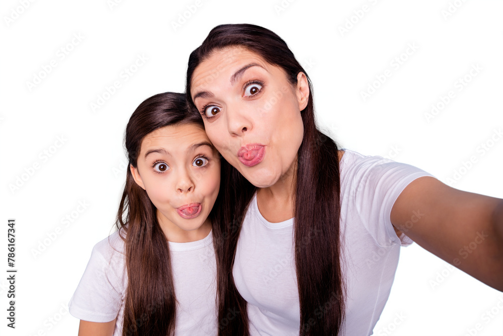 Close up photo amazing beautiful two people brown haired mum mom small little daughter make take selfies tongue out of mouth straw pipe shape figure wear white t-shirts isolated bright blue background Close up photo amazing beautiful two people brown haired mum mom small little daughter make take selfies tongue out of mouth straw pipe shape figure wear white t-shirts isolated bright blue background