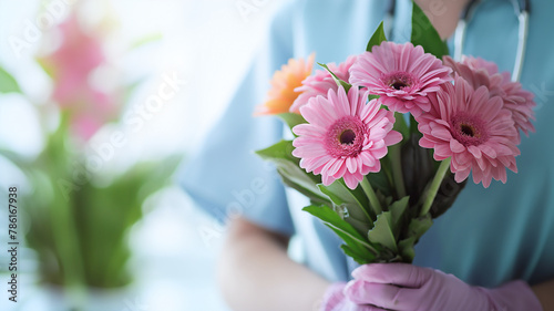 Person in blue scrubs holding a bouquet of pink gerbera daisies  with a soft-focus background.