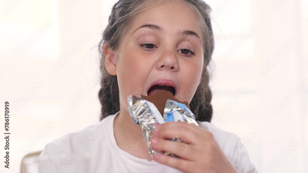 child eating chocolate. unhealthy a food for children sweets concept. grimy girl eating a chocolate bar in the kitchen indoors. kid girl daughter lifestyle eats chocolate against the background child eating chocolate. unhealthy a food for children sweets concept. grimy girl eating a chocolate bar in the kitchen indoors. kid girl daughter lifestyle eats chocolate against the background