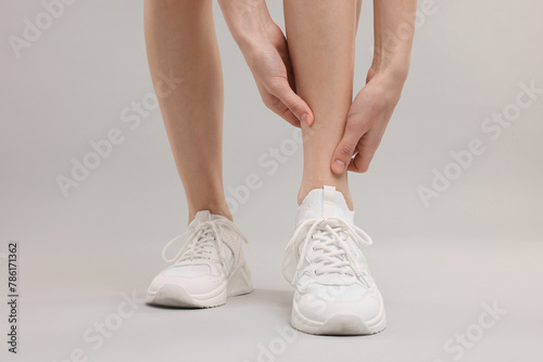 Woman suffering from leg pain on grey background, closeup