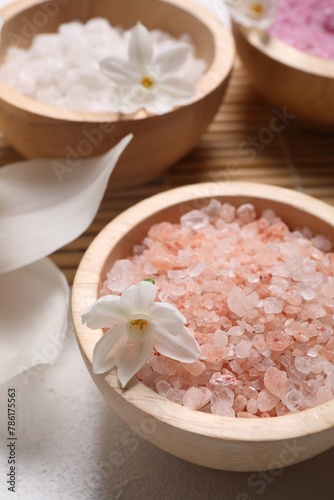 Different types of sea salt and flowers on light table, selective focus. Spa products