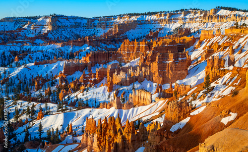 Bryce Canyon National Park in Utah (USA). Giant natural amphitheater panorama at sunrise on a cold winter morning. “Hoodoo“ structures, formed by frost and stream erosion with snow and warm light.